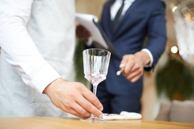 Garsonun yakın çekim restoran yöneticisi gözetiminde masaya bir şarap kadehi koyar