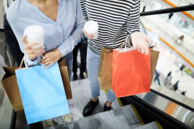İçecekler ve üst katta modern Ticaret Merkezi içinde yürüyen merdiven üzerinde alışveriş sırasında hareket ederken paperbags sohbet kızlarla