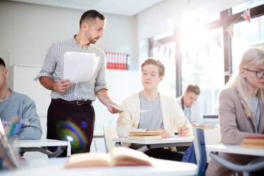 Teacher showing one of students paper with essay or test while passing them over