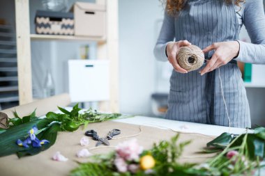 Çağdaş çiçekçi çiçek ve yaprakları ile masa üzerinde iplikleri makara tutan