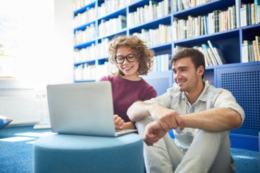 Birkaç sınıf arkadaşı yerde oturuyor ve kütüphanede birlikte dizüstü bilgisayar kullanıyor