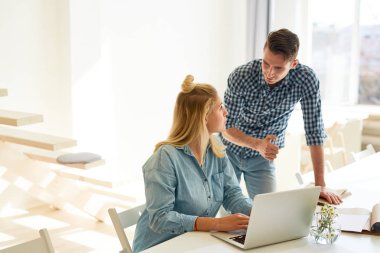 Gündelik giyimli iki genç ofis çalışanı çalışma anlarını tartışıyor