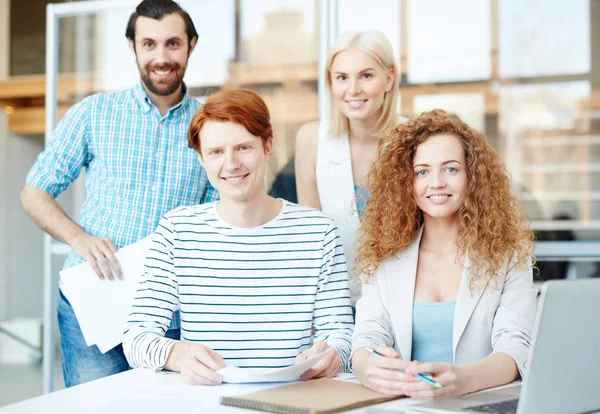 Happy young staff in casualwear looking at camera by their workplace in office