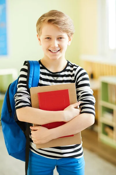 快乐兴奋自信的小学生拿着工作簿 站在教室里对着镜头微笑 — 图库照片