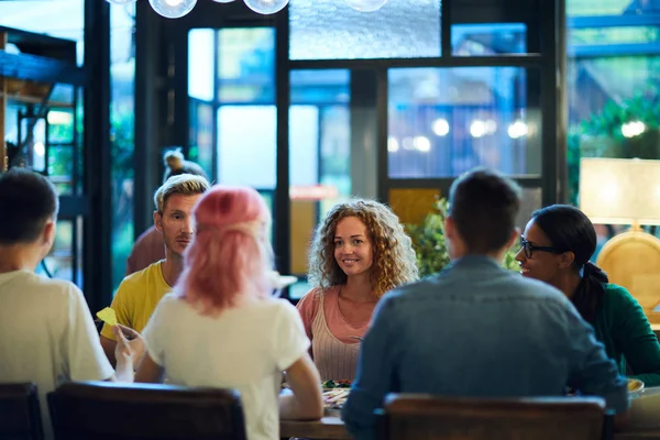 おしゃべりやディナーのためにカフェのテーブルに集まった幸せな異文化の若い友人たち — ストック写真