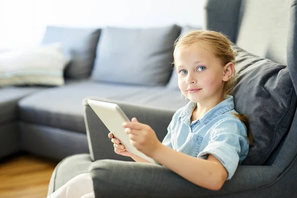 年轻姑娘 带着平板电脑坐在客厅的沙发上 一边看你的网上视频 一边看着你 — 图库照片