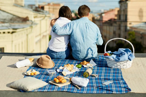グループの若いカップルの背面図屋根の上に座ってテーブルクロスで街並みを眺め 後ろに食べ物を添えた — ストック写真