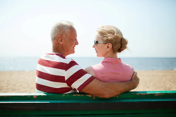 老人抱着妻子 而两人都坐在海边的板凳上 互相看着对方 — 图库照片