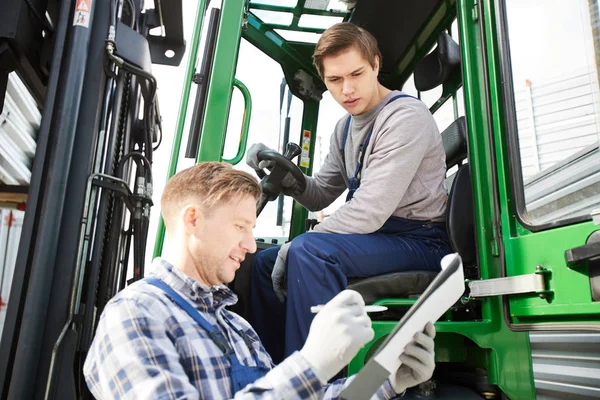 Young driver of load transportation machine looking at foreman checking data in document