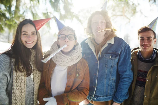 四个快乐的年轻人在美丽的森林户外庆祝圣诞节 他们都戴着派对帽 — 图库照片
