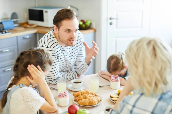 Nervous man sitting by served table and having argument with his wife with two daughters near by