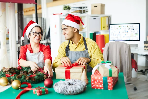 Two Young Colleagues Santa Caps Tying Red Ribbons Wreath Giftbox — Stock Photo, Image