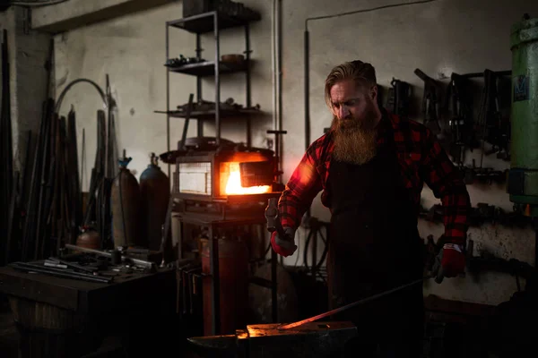胡子专业铁匠用锤子锻造铁工件的热端在铁锤 — 图库照片