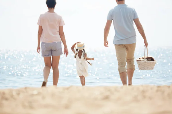 夏の週末に輝く海に向かって砂浜を歩く3人の家族の背面図 — ストック写真