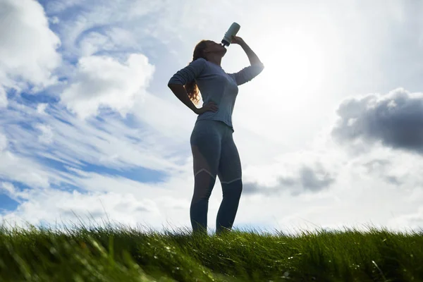 活跃的女孩在棉腿和套头衫喝水对多云的天空锻炼后 — 图库照片