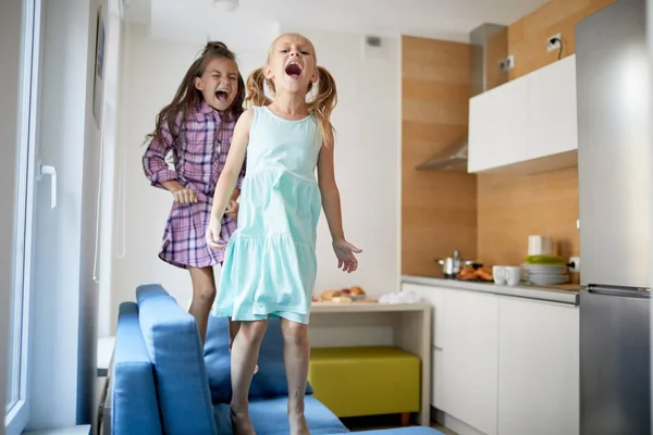 Дві Маленькі Грайливі Дівчата Голосно Кричать Стрибають Дивані Вдома Розважаючись — стокове фото