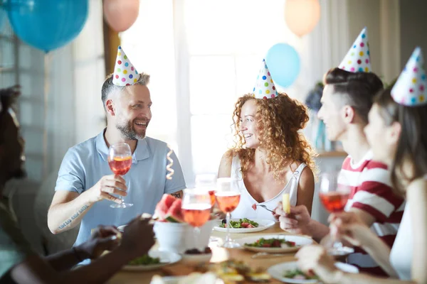 Happy Friends Czapki Urodzinowe Siedząc Przy Świątecznym Stole Toast Ciesząc — Zdjęcie stockowe