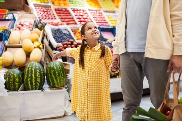面带微笑的漂亮女孩穿着格子裙指着西瓜 要求爸爸在新鲜食品市场买西瓜 他们一边牵着手走过商店 — 图库照片