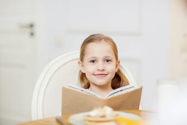 Usměvavá Roztomilá Dívka Dívala Kameru Seděla Stolu Při Čtení Knihy — Stock fotografie
