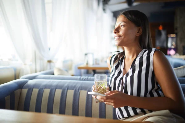 カフェに座っている若いリラックスした女性は スマートフォンでメッセージを通して飲み物やコミュニケーションを取っています — ストック写真