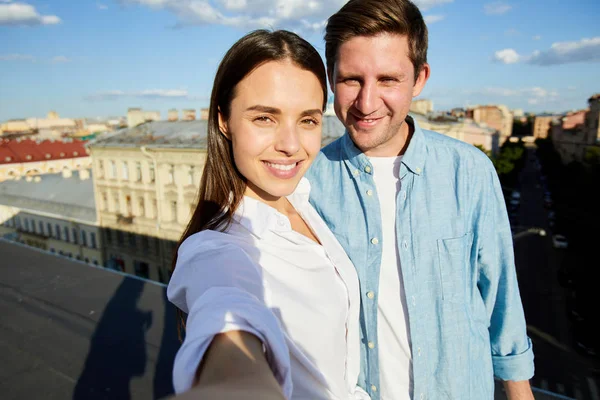 自拍积极美丽的年轻夫妇穿着休闲衬衫微笑着在镜头 而站在城市的屋顶上 游客的概念 — 图库照片