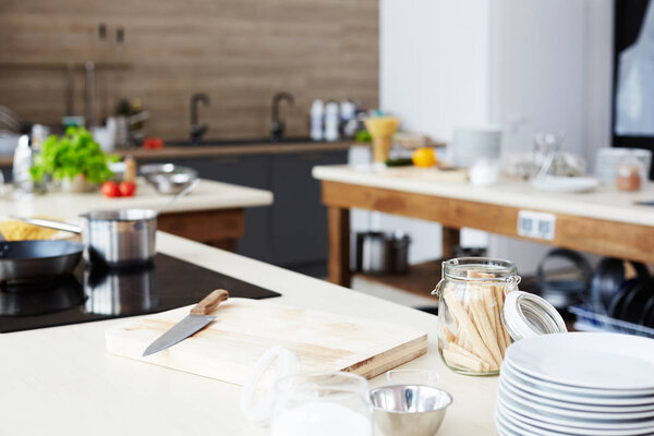 Modern workplace of cooking show: kitchen counter with cutting board, kitchen knife, open glass jar, stack of plates and bowl