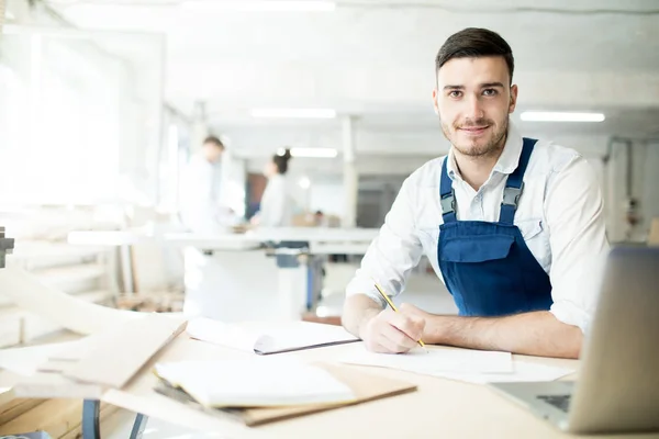 Ingeniero Joven Ropa Trabajo Mirándolo Mientras Está Sentado Lugar Trabajo — Foto de Stock