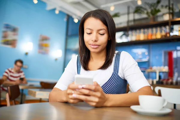 スマートフォンでカフェやメッセージでテーブルに座ってスマートカジュアルの若いビジネス女性 — ストック写真
