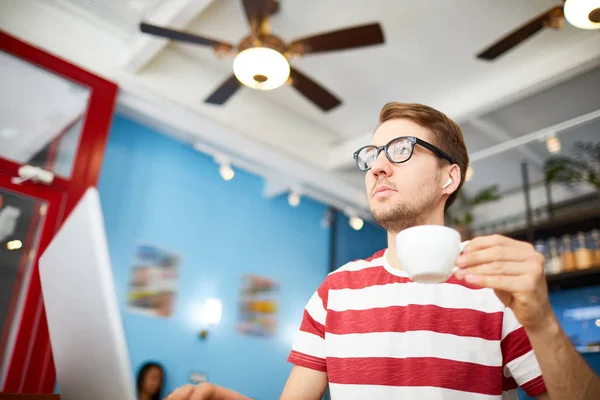 コーヒーブレイク中にラップトップの前のカフェに座って飲み物のカップを持つ深刻なビジネスマン — ストック写真