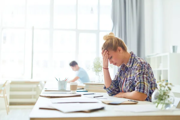 Young tired or troubled businesswoman leaning over paper while reading it or trying to concentrate