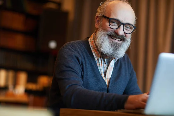快乐的胡子老人在眼镜打字在笔记本电脑上 而浏览在网上 — 图库照片