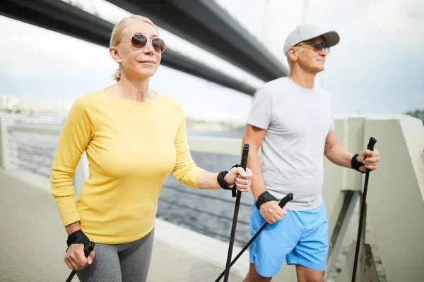 Sportliches Älteres Paar Aktivkleidung Bewegt Sich Mit Trekkingstöcken Entlang Der — Stockfoto