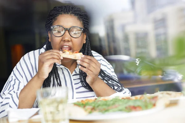 カフェで昼食を楽しみながら食欲をそそるピザのスライスから口を開く空腹の混合人種の女性 — ストック写真