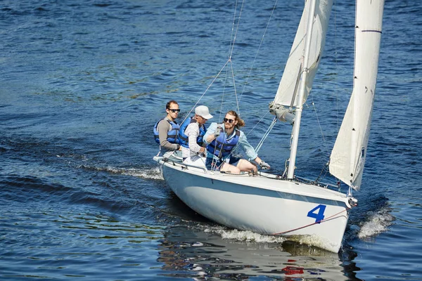 一群戴着太阳镜和救生衣的自由游艇手坐在帆船甲板上 在比赛时四处观景 — 图库照片