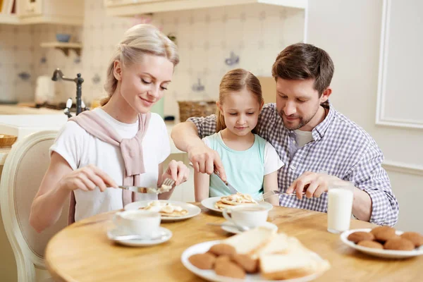 朝の朝食を食べるカジュアルな服装で幸せなコンテンツフレンドリーな家族 若い父親は ダイニングルームでパンケーキをカットする娘を支援 — ストック写真