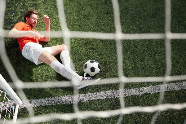 ゲートで緑の草原に横たわっている間足でサッカー ボールを捉える若いゴールキーパーの平面図 — ストック写真