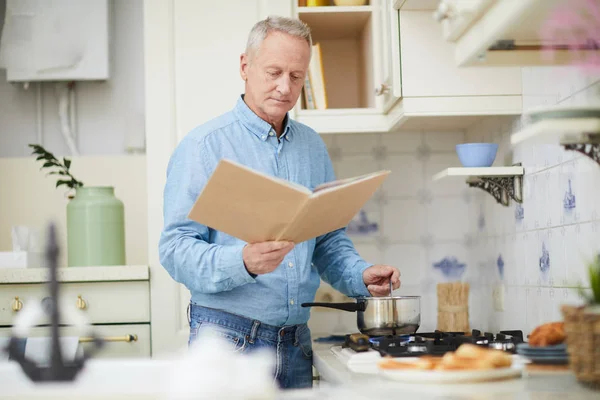 Reifer Mann Mit Offenem Kochbuch Steht Herd Und Mischt Etwas — Stockfoto