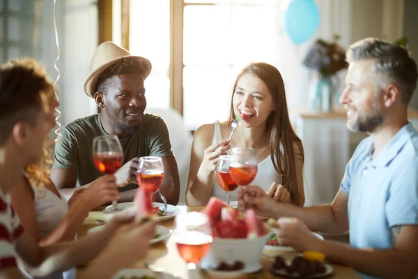 ホームパーティー中にお祝いのテーブルで誕生日の食べ物を楽しむ幸せな若いゲスト — ストック写真