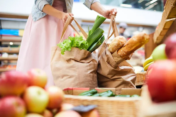 Close-up of unrecognizable woman in skirt standing in food organic store and picking heavy shopping bags full of products