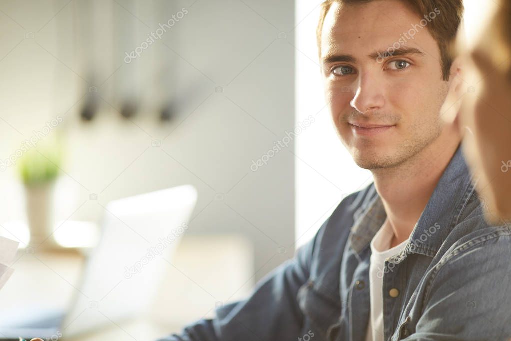 Warm toned portrait of handsome young man wearing casual clothes smiling while listening to colleague during meeting, copy space