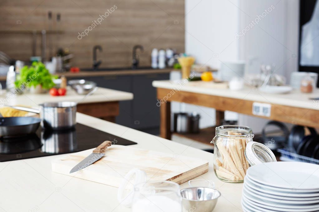 Modern workplace of cooking show: kitchen counter with cutting board, kitchen knife, open glass jar, stack of plates and bowl