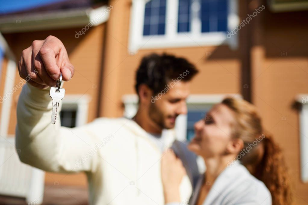 Young man showing key of new house while looking at his wife outdoors