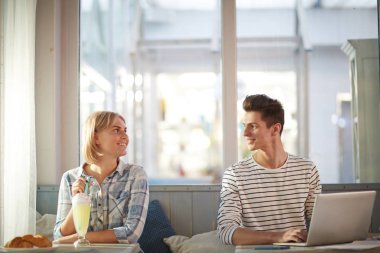 Mutlu adam dizüstü bilgisayarda yazarak ve kafede vakit geçirirken tatlı kokteyl sahip kız arkadaşı bakarak