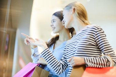 İki genç alışveriş yeni moda koleksiyonu bir vitrin tarafından dururken bölümlerin tartışıyor
