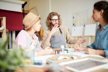 Stüdyoda masa başında oturan genç öğrenciler toplantıda yaratıcı fikirleri tartışıyorlar.