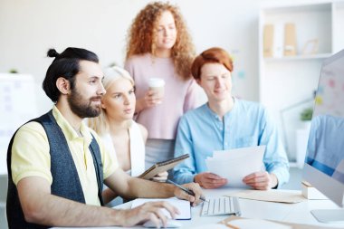 Masa başı oturan, çevrimiçi verilere bakan ve yeni eğilimleri tartışan bir grup genç tasarımcı