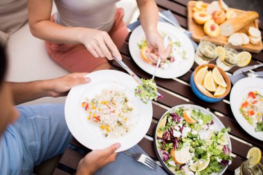 Genç bir kadın kafede öğle yemeği sırasında erkek arkadaşının tabağından taze sebze salatası alıyor.