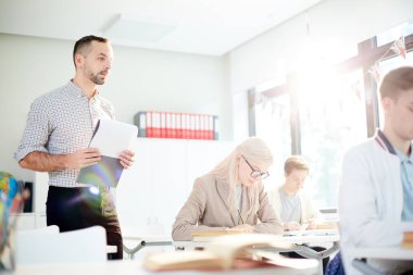 Öğrenciler derste yazılı görevi yerine getirirken, belge li öğretmen satırlar boyunca yürüyor