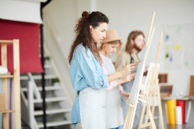 Stüdyoda resim dersinde şövalelerinin önünde duran genç öğrenciler sırası