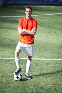 Çapraz kolları bacakları biri futbol topu yeşil alan üzerinde dururken tutmak olan genç adam
